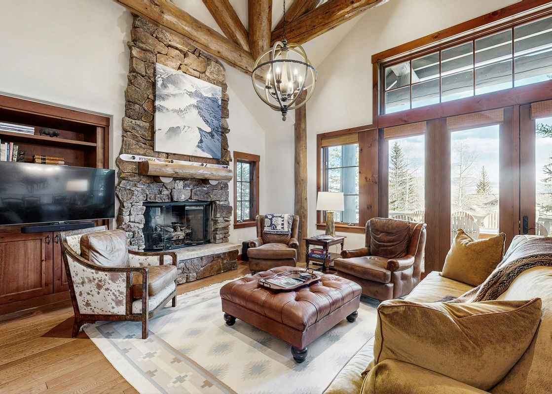 A cozy living room in The Gulch Getaway features a large stone fireplace, comfortable leather seating, and a TV, with big windows offering outdoor views.