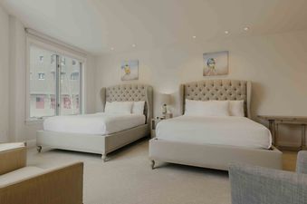 A spacious bedroom at Sanctuary Chalet at One Beaver Creek, featuring two queen-sized beds with tufted headboards, white bedding, and two matching bird paintings above each bed.