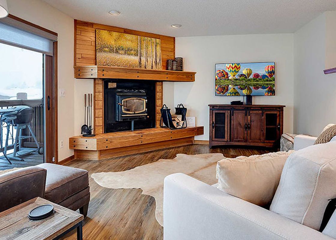 A cozy living room at Ranch at Steamboat RA203 with a fireplace, TV, and balcony access with a BBQ grill, showcasing a snowy mountain view.