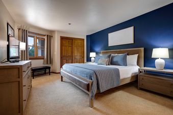 A king-sized bed with a leather frame and blue bedding sits against a navy accent wall in a luxurious bedroom at Chateau Chamonix CX113.