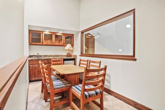 A dining table with four chairs and a wet bar area with cabinets and a mini-fridge.