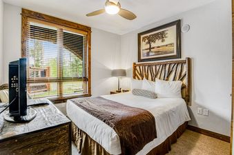Cozy bedroom with a queen bed, rustic branch headboard, and a large window with blinds at BlueSky Breckenridge 409.