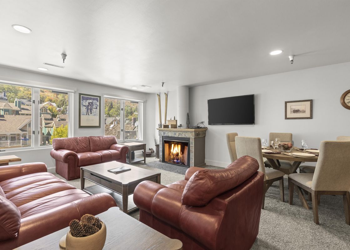 The living area at Fashion Coalition 402 features two large red leather sofas, a stone fireplace, a flat-screen TV, and an adjacent dining area.