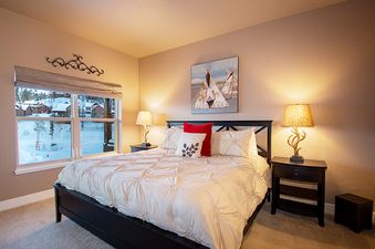 A cozy bedroom with a large bed, two nightstands with lamps, and a window overlooking a snowy landscape.