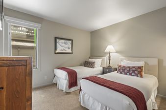 A cozy bedroom at Snow Flower 140 Park City with two twin beds, a wooden nightstand, and a framed mountain painting on the wall.