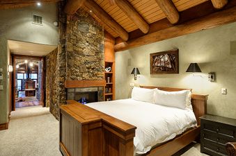 A cozy, rustic-chic bedroom at Treehouse on West Fork with a stone fireplace, wood-beamed ceilings, and a comfortable bed.