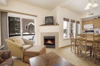 A cozy living room in Winterstar G3 featuring a comfortable armchair, a fireplace, and a dining area, with a view of a snowy outdoor landscape through a sliding glass door.