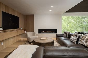 A luxurious living room at Onyx Lodge features a dark leather sectional, a modern fireplace, and a large window with green outdoor views.
