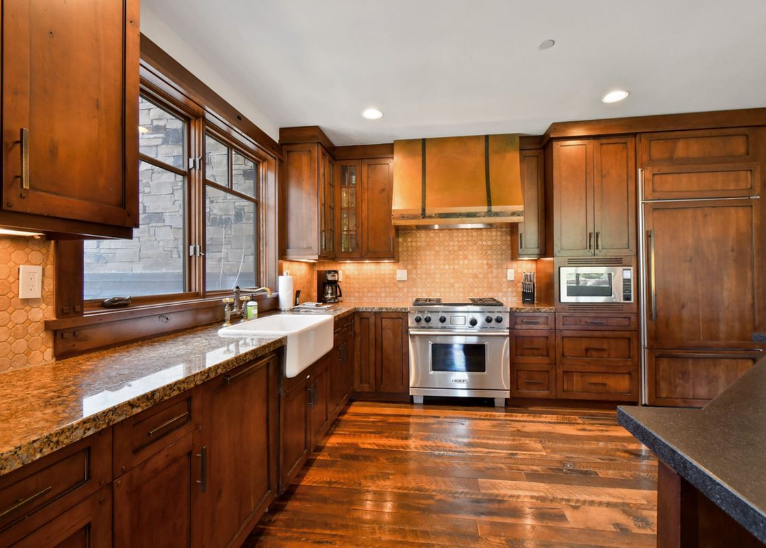 A rustic yet modern kitchen with rich wooden cabinetry, granite countertops, stainless steel appliances, and a farmhouse sink.
