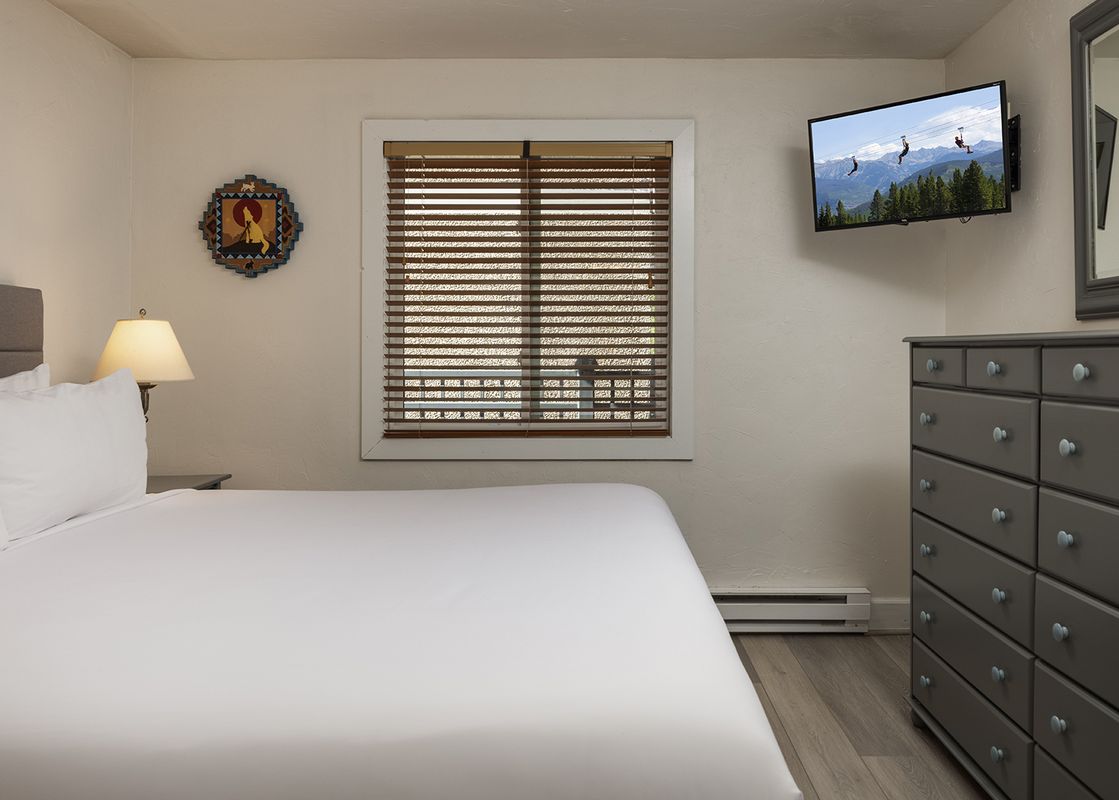 A cozy bedroom at Vantage Point 501 features a king-size bed with white linens, a bedside lamp, a dresser, and a wall-mounted TV.