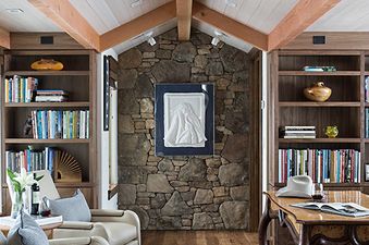 A cozy study at the Paintbrush Retreat with vaulted ceilings, a stone wall, bookcases, and comfortable armchairs.