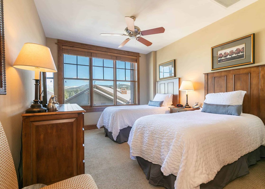 Two twin beds in a hotel room with white linens and a view of a mountainside landscape outside the window.