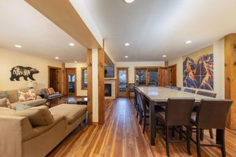 The River House Lodge features a spacious open-concept living area with comfortable seating, a dining table for large gatherings, and a cozy fireplace, all under warm lighting.