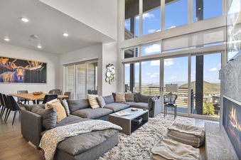 A spacious living room at Apex 1501 featuring a large sectional sofa, a modern fireplace, an adjacent dining area, and floor-to-ceiling windows revealing panoramic mountain views.