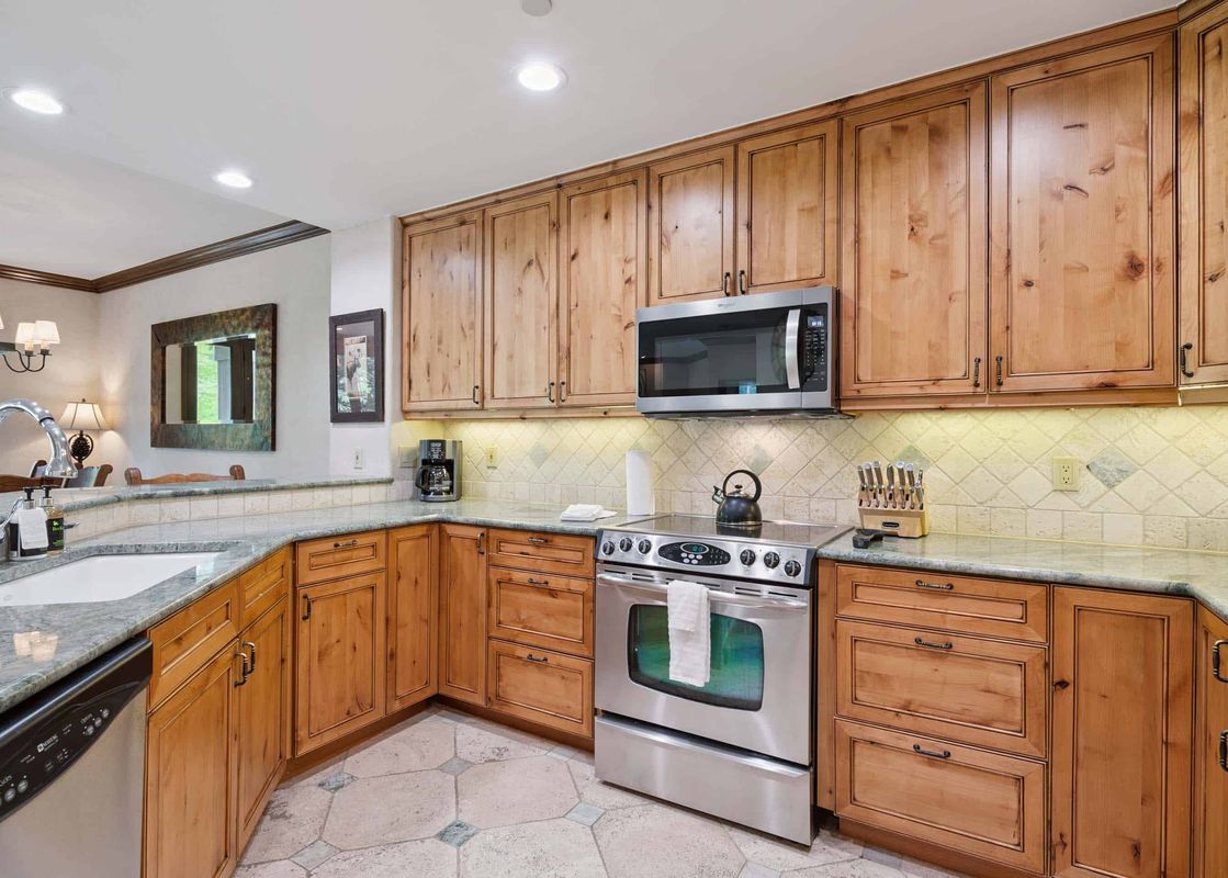 A well-lit kitchen featuring light-colored wooden cabinetry, granite countertops, and stainless steel appliances.