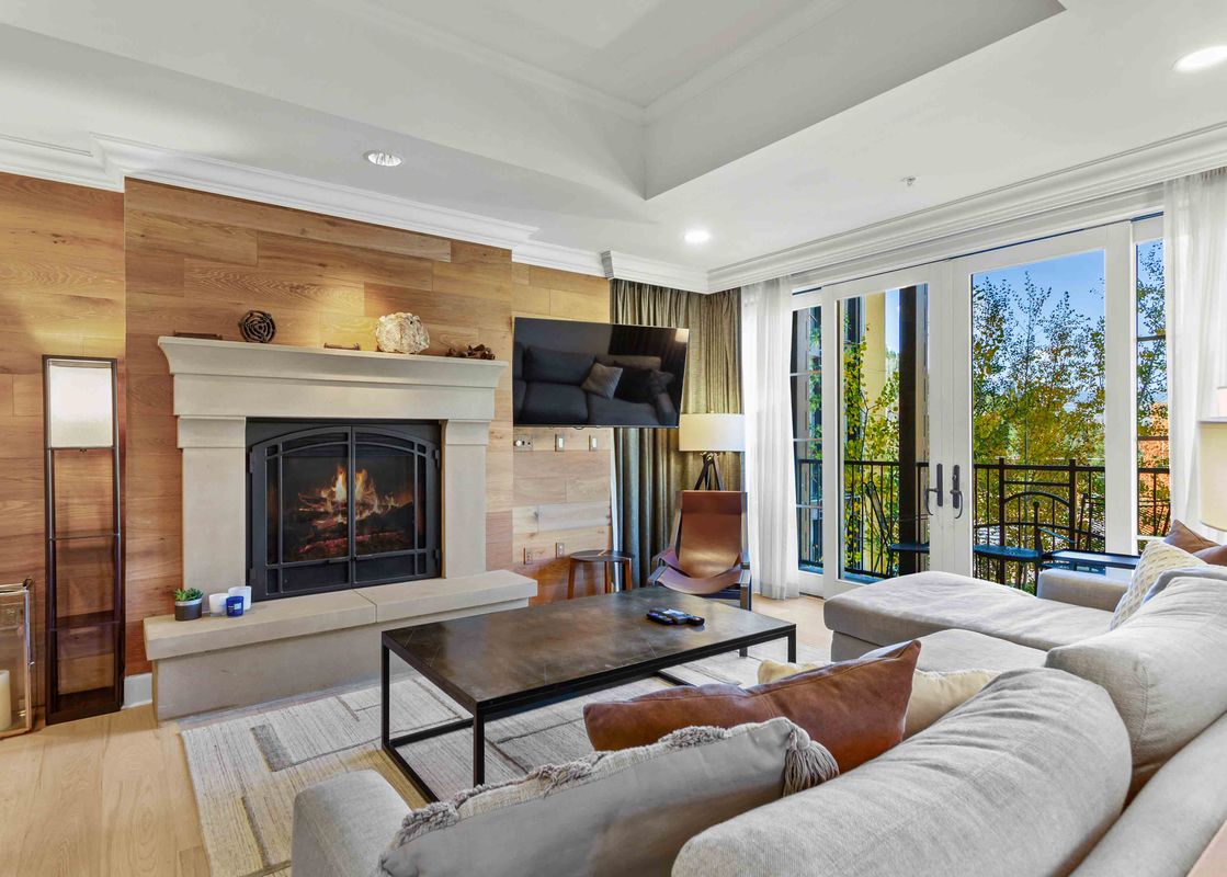 A living room with a fireplace, a couch, and a large window with a view of trees.