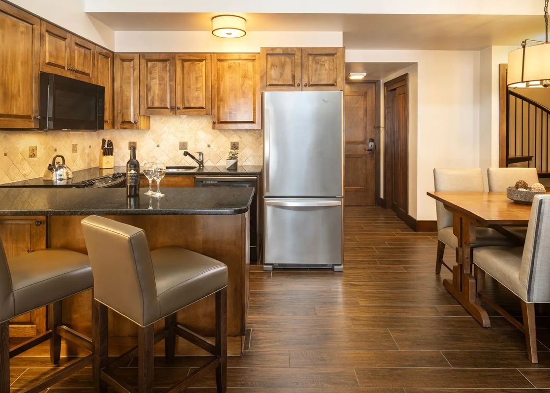 Fully equipped kitchen with wooden cabinetry, stainless steel appliances, breakfast bar, and adjoining dining table.
