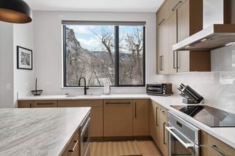 A modern kitchen in One Riverfront Townhome 05 with light wood cabinets, white countertops, and a large window looking out onto a snow-covered mountain landscape.