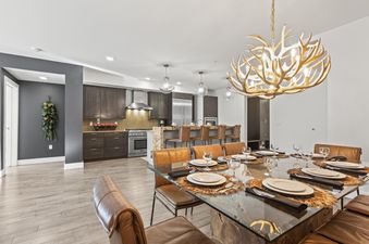 A modern dining area with a glass-topped table and brown leather chairs, featuring an antler-style chandelier, opens to a kitchen with dark wood cabinets and stainless steel appliances in Rio Grande 203 204.