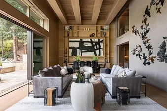 The great room of the Opus Estate features soaring wooden ceilings, plush grey sofas, a large abstract painting, and a unique 3D wall art installation.