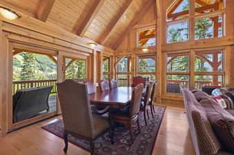 A spacious dining area at Rested Ridge Ski Haus with a large wooden table, comfortable chairs, and panoramic mountain views through expansive windows.