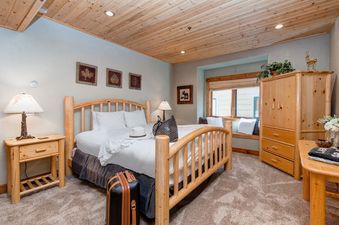 A cozy bedroom at Bristlecone Deer Valley features a wooden bed frame and plenty of natural light.