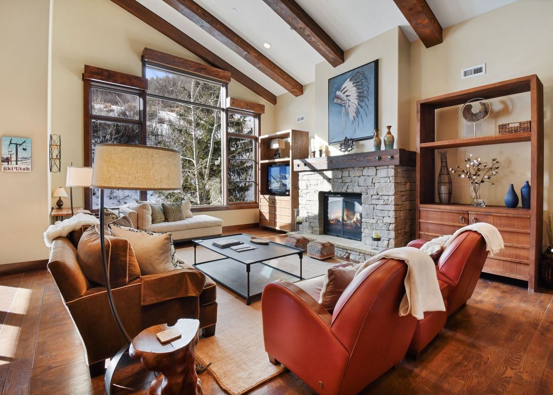 A cozy living room with a fireplace, comfortable armchairs, and large windows offering a view of a snowy landscape.