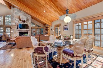 A dining area with a large glass table and chairs, an ornate rug, and a stone fireplace in the background.
