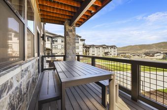 A modern balcony with a dining table and benches, overlooking a residential area and mountains under a blue sky.