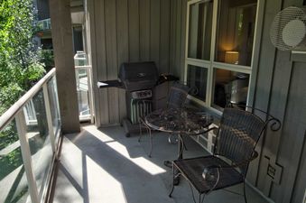 The private balcony at Aspens on Blackcomb Unit 304 features a barbecue grill and a bistro table set with two chairs, surrounded by lush green foliage.