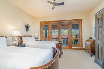 A luxurious bedroom at TRISTANT 115 with two elegantly framed beds, dark wood furniture, and glass doors leading to a balcony with mountain views.