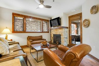 The living room at BlueSky Breckenridge 410 featuring a stone fireplace, flat-screen TV, comfortable seating, and rustic decor.