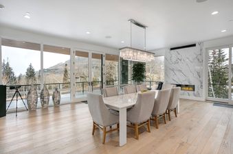 The dining room at Quicksilver Haus with a white marble dining table, light-colored chairs, a crystal chandelier, and a marble fireplace with mountain views.
