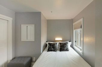 A cozy bedroom at Blue Mesa 20a with a bed, decorative pillows, a wall-mounted light, a window with blinds, a mirror, and a grey ottoman.