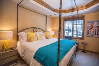 A luxurious bedroom at Chateau Beaver Creek Residence 1304, featuring a four-poster bed with colorful bedding and a large window overlooking a snowy exterior.
