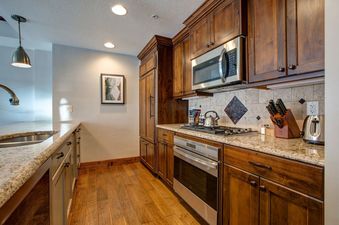The kitchen in Abode at First Dawn A features wood cabinets, granite countertops, and stainless steel appliances.