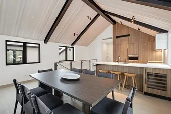 Dining area and kitchen inside the Maison Cornet with modern wood finishes and vaulted ceiling.