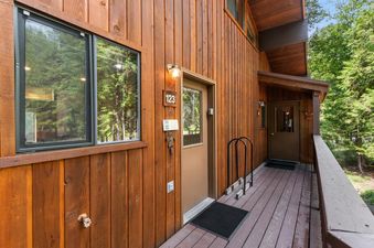 The exterior entrance of Ptarmigan Hideout is shown, featuring a wooden facade, windows reflecting green trees, and the unit number 123 displayed next to the front door.