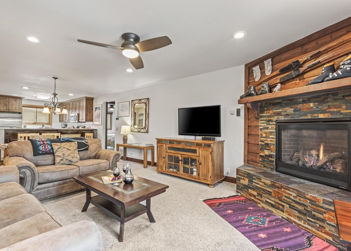 A cozy living room in Snow Flower 56 Park City with a stone fireplace, brown sofas, a wooden coffee table, and a TV on an entertainment console.