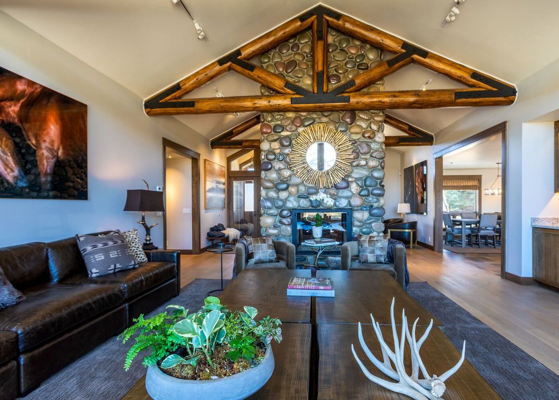 The living area of Abode at Sage Springs features a large stone fireplace, exposed wooden beams, and comfortable seating, with a large horse painting on the wall.