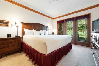 A hotel bedroom with a king-size bed, nightstands, and french doors that lead to a view of the outdoors.