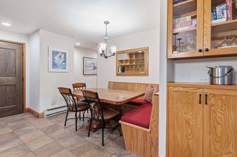 A cozy dining area at The Charter E2105 with a wooden table, built-in bench seating with red cushions, and additional chairs, illuminated by a chandelier and decorated with a mirrored shelf.