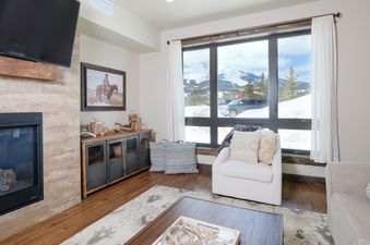 The living area of Mountain Lake Condo 101B features a fireplace, a smart TV, and a large window offering mountain views.