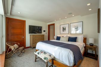 A master bedroom at Le Chamois Penthouse offers a king-sized bed, a flat-screen TV, a dresser, and a seating area with a wicker chair.