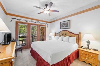 A king bedroom at The Charter A3505 with a wooden headboard, a white duvet, and a red bed skirt. French doors open to an exterior view.