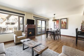 A spacious living and dining area in Lowell 204 featuring a fireplace, a dining table, comfortable seating, and large windows with an exterior view.