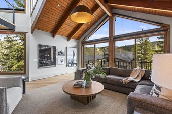 A spacious and inviting living area in Pinnacle in Deer Valley, featuring a large sectional sofa, a round wooden coffee table, and an expansive window offering picturesque mountain views.