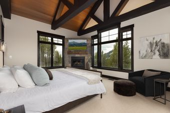The master bedroom at Summit View Chalet Big Sky features a king bed, fireplace, television, and stunning mountain views from large windows.