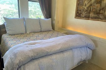 A bed with white linens and a patterned comforter, with a window view of mountains and trees.