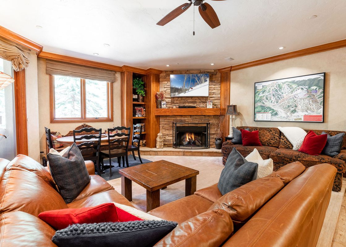 A cozy living room with a fireplace, two leather couches, a coffee table, and a large ski map on the wall.